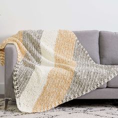 a couch with a blanket on top of it next to a rug and potted plant