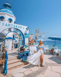 a woman in a white dress sitting on some steps near the ocean with an umbrella