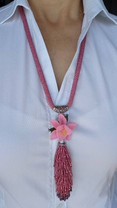 a woman wearing a white shirt with a pink flower and tasseled necklace on her neck