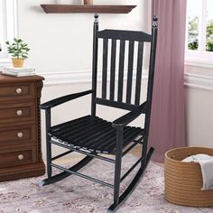 a black rocking chair sitting on top of a rug next to a dresser and window