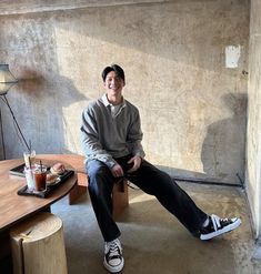 a man sitting on top of a wooden bench in a living room next to a table