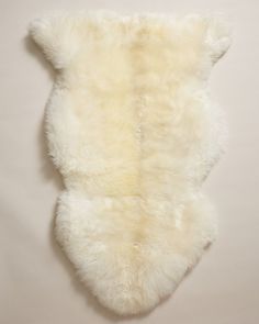 a white sheepskin rug is laying on the floor in front of a beige wall