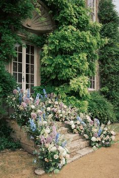 an old house with flowers and ivy growing on the outside wall, along with stone steps leading up to it's front door