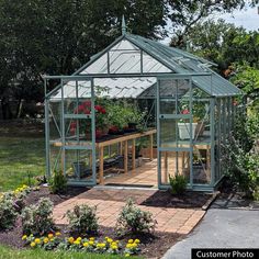 a green house sitting on top of a lush green field next to flowers and trees