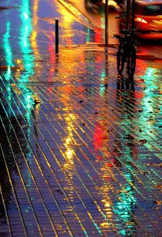 a city street at night with cars and lights reflecting off the wet pavement in the rain