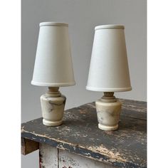 two lamps sitting on top of a wooden table next to each other with white shades