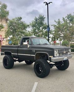 a large black truck parked in a parking lot next to a street light and trees