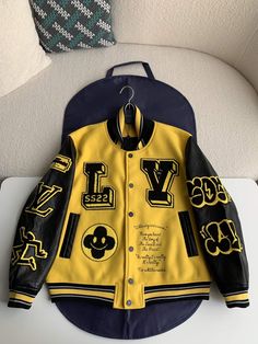 Embrace a bold and playful spirit in a vibrant yellow hue with this LV-inspired Embroidered Varsity Jacket. This statement piece reimagines the classic silhouette with luxurious details and a touch of contemporary flair. The soft woolen body contrasts beautifully with the supple cowhide sleeves, creating a textural interplay. The iconic LV signatures and a playful panther motif patch on the back add a touch of personality, while the leather piping on the pockets, snap fastenings on the front, an Spring Varsity Jacket With Embroidered Graphics, Trendy Fall Outerwear With Embroidered Graphics, Yellow Graphic Print Outerwear For Streetwear, Casual Yellow Outerwear With Letter Print, Yellow Graphic Print Outerwear For Spring, Spring Yellow Outerwear With Graphic Print, Fall Yellow Letter Print Outerwear, Yellow Varsity Winter Outerwear, Yellow Varsity Outerwear For Winter