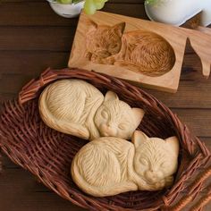 three carved cats sleeping in a basket next to a wooden cutting board and vase with flowers