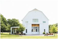 a large white barn sitting in the middle of a lush green field next to trees