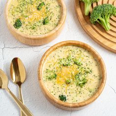 broccoli and cheese soup in wooden bowls with spoons next to it on a white surface