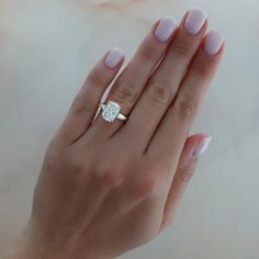 a woman's hand holding a ring with a diamond on it and the middle finger