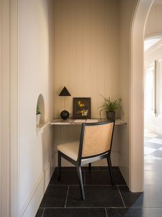 a chair sitting on top of a black tile floor next to a white table with a potted plant