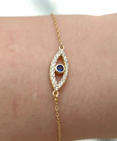 This is an elegant bracelet made with a fine gold chain and a center piece in the shape of an eye known as the "evil eye" or "eyes against lessons". The centerpiece is encrusted with small sparkling stones and has a blue stone in the center, symbolizing protection against the evil eye and negative energy. The bracelet is a stylish and delicate accessory that not only adds beauty, but also brings empathic protection to its wearer. material: 925 silver and 14 carat gold  evil eye size: 22mm. / 0.8 Elegant Evil Eye Bracelet With Diamonds As Gift, Elegant Gold Evil Eye Bracelet With Diamond Eyes, Elegant Gold Evil Eye Bracelet With Diamond Details, Elegant Gold Plated Evil Eye Bracelet, Elegant Sterling Silver Evil Eye Bracelets, Elegant Evil Eye Bracelet With Adjustable Chain, Elegant Evil Eye Bracelet With Adjustable Chain Gift, Elegant Beaded Evil Eye Bracelet, Elegant Gold-plated Evil Eye Bracelet Gift