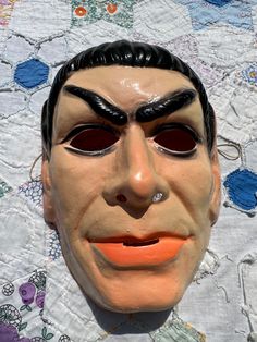 a close up of a person wearing a mask on top of a quilted table cloth