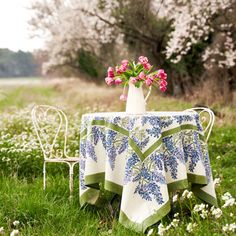 a table with a vase and flowers on it in the middle of a grassy field