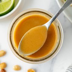 a spoon in a jar filled with peanut butter next to peanuts and lime wedges