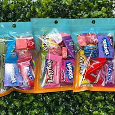 three bags of candy sitting next to each other on top of a green plant filled with leaves