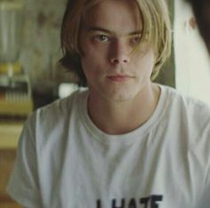 a young man with blonde hair wearing a white shirt and looking at another person's face