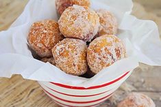 powdered sugar donuts in a red and white striped bowl on a wooden table