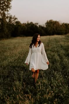 a woman in a white dress walking through tall grass