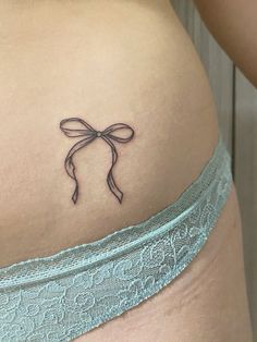 a woman's stomach with a small bow tattoo on her left side ribcage