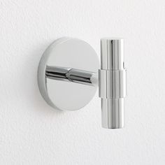 a chrome wall mounted toilet paper dispenser on a white wall with a circular handle