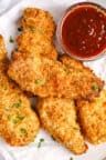 some fried food on a white plate with ketchup and dipping sauce in the background