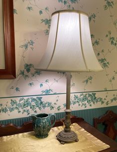 a table with a lamp on top of it next to a mirror and wall paper