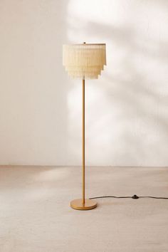 a floor lamp with a beige shade on the base and a white wall behind it