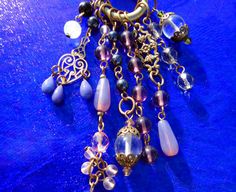 Art Nouveau inspired plum, lavender, and deep purple gems create a fresh lush pendant.  Cascading from a bold one inch brass ring are multi shapes and sizes of amethyst, agate, clear crystal quartz, hematite, with floral and heart charms.  This 4 inch long Boho style pendant is Artisan Handcrafted in America and has a 36 inch black silk cord that can easily be made shorter.  If you prefer, I am happy to custom make a chain with gemstones, or other colored silk or leather cord.  Enjoy! Inv #  P425 Retail $98 SHOP POLICIES: QUALITY & VALUE: Fresh Jewels are Artisan Handcrafted in America, designed to enjoy wearing for a lifetime, and may become a cherished heirloom. Prices here are up to 75% OFF prices compared to Designer Stores and Boutiques! Every Jewel is backed with a Quality Guarantee, Purple Gems, Silk Cord, Statement Pendant, Brass Ring, How To Make Shorts, Clear Quartz Crystal, Boho Stil, Inspiration Art, Crystal Quartz