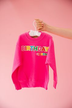 Be the reigning Birthday Queen in this MINI KIDS pink pullover. With colorful patches adorning the front, you'll rule the party in style. A must-have for any mini fashionista, this pullover is the perfect mix of playful and chic. Long live the Queen! This is a made-to-order item. All customized orders are currently shipping within 14 business days. To receive item quicker, expedited shipping is available at checkout. Pink Crew Neck Top For Birthday, Pink Crew Neck Top For First Birthday, Pink Long Sleeve Top For Birthday, Trendy Pink Tops For Birthday, Pink Long Sleeve Birthday Sweatshirt, Pink Long Sleeve Sweatshirt For Birthdays, Pink Long Sleeve Sweatshirt For Birthday, Playful Pink Top For First Birthday, Playful Pink Tops For First Birthday