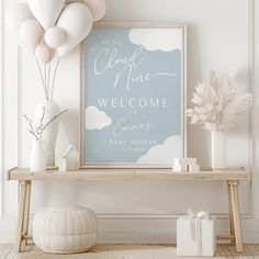 a baby shower welcome sign with balloons in the background and a white vase filled with flowers