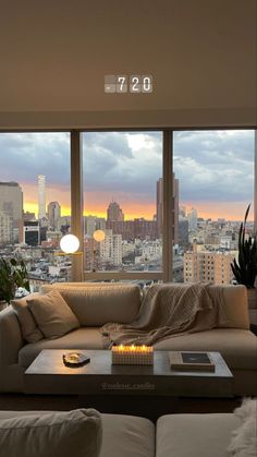 a living room filled with furniture and a large window overlooking the cityscape at sunset