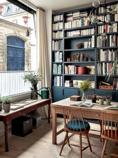 the room has many bookshelves and desks with chairs in it, along with two windows that look out onto an alley