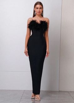 a woman standing in front of a white wall wearing a black dress with feathers on it