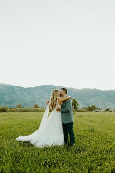 a bride and groom embracing in the middle of a field with mountains in the background