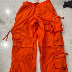 Baggy Parachute Pants With Side Panel Pockets. Adjustable Ruched Gathered Drawstring Hem. 100% Polyester. Size Xs Color Is Orange. Worn Twice Excellent Condition Baggy Nylon Parachute Pants With Drawstring, Summer Streetwear Parachute Pants With Side Pockets, Summer Streetwear Cargo Pants With Drawstring, Orange Bottoms With Pockets For Outdoor, Summer Nylon Cargo Pants With Cargo Pockets, Techwear Parachute Pants For Summer Streetwear, Summer Techwear Parachute Pants For Streetwear, Summer Streetwear Nylon Parachute Pants, Sporty Orange Bottoms With Drawstring