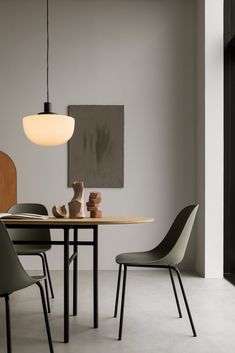 a dining room table with chairs and a vase on the top, in front of a gray wall