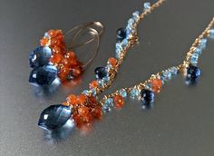 "This unique set shimmers with vibrant blues and orange, perfect for summer parties, adding a festive touch to any outfit. The matching necklace and earring design feature gemstones of London blue quartz colour, orange carnelian and light blue aqua chalcedony which cascade from their elegant wire-wrapped design in a chandelier style. This stunning set are sure to dazzle with their eye-catching colours, glittering with their elegant beauty. The necklace features a large 15mm London blue quartz co Blue Briolette Jewelry For Party, Blue Carnelian Jewelry For Gifting, Blue Carnelian Jewelry For Gift, Blue Carnelian Jewelry As A Gift, Blue Carnelian Jewelry Gift, Handmade Blue Carnelian Jewelry, Chalcedony Necklace, Orange Carnelian, Gold Topaz