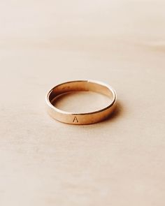 a gold wedding ring with the letter a on it sitting on a beige table top