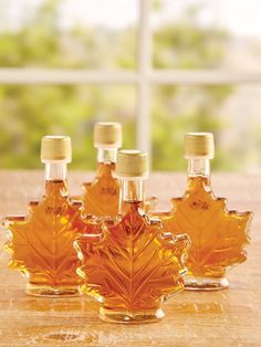 three maple leaf shaped glass bottles sitting on top of a wooden table next to a window