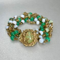 "Vintage Miriam Haskell Green Bracelet, Gold tone Multi Strand Jade Glass Bead Bracelet, Midcentury Collectible Signed Jewelry, Gift for Her. Era: Around 1950- 1951. Designer Signed: Miriam Haskell. Measurements: - Length Around Wrist : 8 1/2\" - Width: 1 1/2\" Details: -Metal Color: Gold - Embellishments: Gold Tone Plating, Pendant with Light Green Glass Stone in the middle. Five gleaming Strands of small Round Beads that are linked in-between by tiny Gold beads strands. Glass Beads: imitation Vintage Gold Beaded Bracelet With Spacer Beads, Elegant Multi-strand Polished Beaded Bracelets, Vintage Polished Beads Bracelet Jewelry, Vintage Polished Beads Bracelet, Vintage Faceted Beads Bracelet, Vintage Polished Bead Bracelet, Vintage Adjustable Bracelet With Polished Beads, Vintage Adjustable Bracelets With Polished Beads, Elegant Multi-strand Hand-strung Bracelet