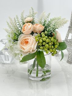 a glass vase with flowers and greenery in front of the eiffel tower