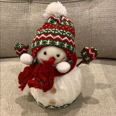 a snowman with a red scarf and hat on it's head sitting on a couch