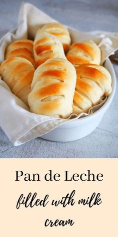 some bread rolls in a white bowl on top of a table with the words pan de leche filled with milk cream