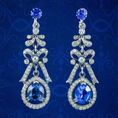 "A fabulous pair of Vintage drop earrings from the mid 20th Century decorated with glistening, brilliant cut white pastes and larger Bristol blue pastes that simulate diamonds and sapphires.  The drop galleries have an Edwardian inspired design and are crafted in a silver base metal with bows in the centre and secure screw back fittings at the top stamped with a \"Continental\" mark. They're very pretty and perfect for a wedding or glamorous occasion.  WEIGHT: 16 grams together MEASURE: Width 20 Blue Diamond-accented Evening Earrings, Classic Blue Diamond Earrings For Wedding, Blue Diamond Drop Earrings For Formal Occasions, Formal Blue Pear-shaped Diamond Earrings, Blue Oval Earrings For Evening, Blue Diamond Earrings For Formal Occasions, Formal Jeweled Blue Earrings, Formal Blue Diamond Earrings For Pierced Ears, Formal Blue Diamond Earrings