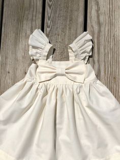 "Beautiful Big Bow Girls dress. Made of 100% cotton, Back has elastic for comfort and a great fit. This dress is a must have for your child's wardrobe. Also makes a beautiful gift! The listing is for one bow dress! These are the APPROXIMATE measurements of my dresses from shoulder to hem: size/chest/length 0-3m / 14\"/13\" 3-6m /16/14\" 6-9m /17\"/15\" 9-12m /18\"/16\" 12m-18m /19\"/17.5\" 18m-24m /20\"/19\" 2t /21\"/20\" 3t /22\"/20.5\" 4t / 23\"/22\" 5t /24\"/23\" 6y / 25\"/24\" 7y / 26\"/25\" Beige Summer Dresses With Bow, Summer Baptism Dress With Bow Detail, Summer Cream Dress With Bow Detail, Summer Cream Dress With Bow, White Bow Dress For First Birthday, White Dress With Bow For First Birthday, Cream Spring Dress With Bow, Fitted White Dress With Bow Tie, White Fitted Dress With Bow Tie