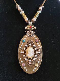 "This listing is for an unsigned cameo pendant necklace that is constructed in half beaded and half chain. The cameo is small and oval shape in a light brown with a white high relief woman facing left. It feels like plastic and is on a nice ornate frame with small white seed beads. Around the frame are colored glass rhinestones in blue, pink and yellow. The top frame is hinged with a beaded wire. Above it is an embossed flower with a red rhinestone and 2 white seed beads to the sides. The bezel Vintage Oval Jeweled Necklaces, Vintage Oval Jeweled Necklace, Vintage Jeweled Oval Necklace, Vintage Oval Beaded Necklace, Metal Embellishments, Cameo Pendant Necklace, High Relief, Cameo Necklace, Cameo Pendant