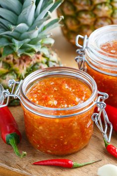 two glass jars filled with salsa sitting on top of a wooden cutting board next to pineapples